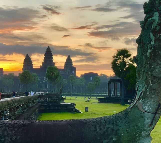 Dramatic golden sunrise over the ancient towers of Angkor Wat with a carved Naga balustrade in the foreground.