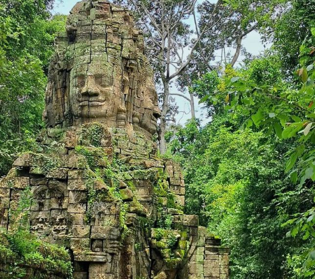 Ancient stone face tower covered in moss at Ta Som temple surrounded by green jungle foliage.