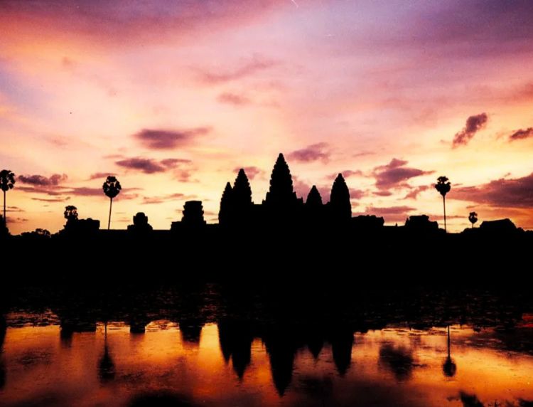 Silhouetted towers of Angkor Wat reflected in the lotus pond during a vibrant sunset