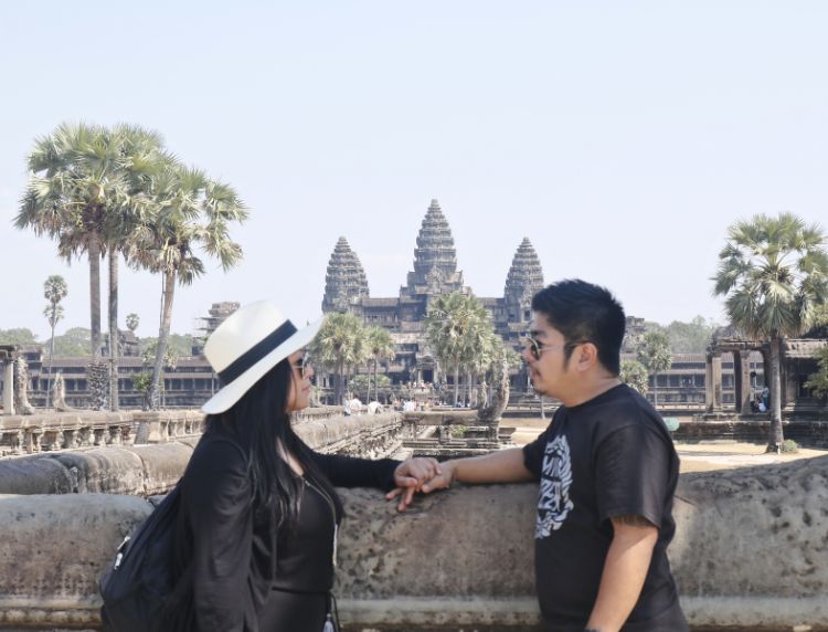 Couple holding hands along the ancient stone causeway facing Angkor Wat towers