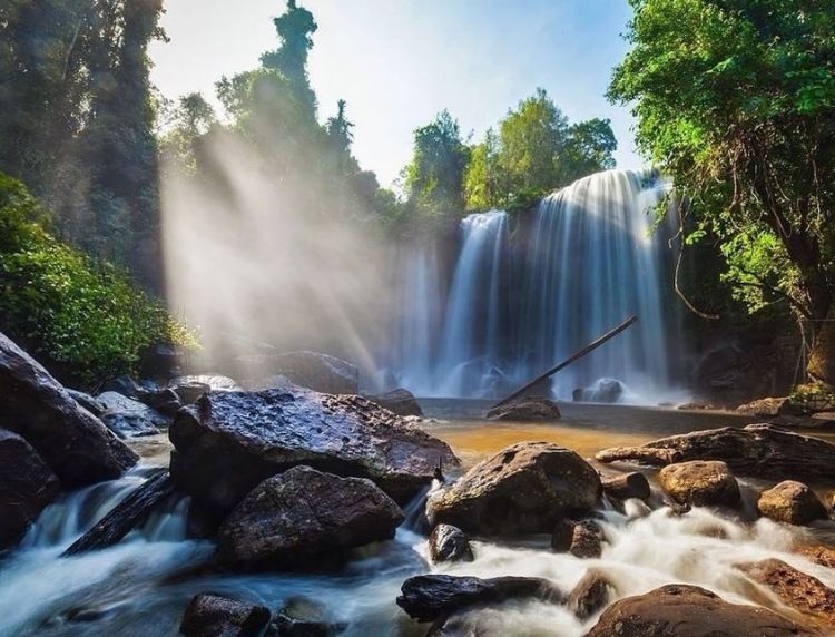A tropical waterfall cascading into a rocky river with sunbeams breaking through the jungle canopy.