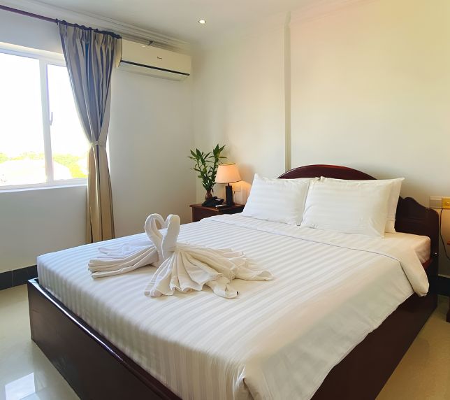 Deluxe double hotel room with a dark wood bed, folded towel swans, white linens, and air conditioning.