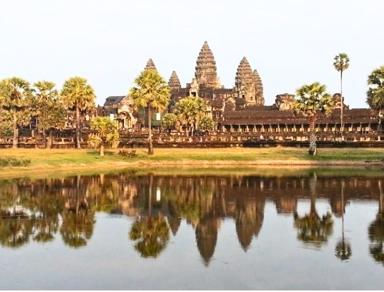 The central towers of Angkor Wat reflected in the calm waters of the outer lily pond during golden hour.