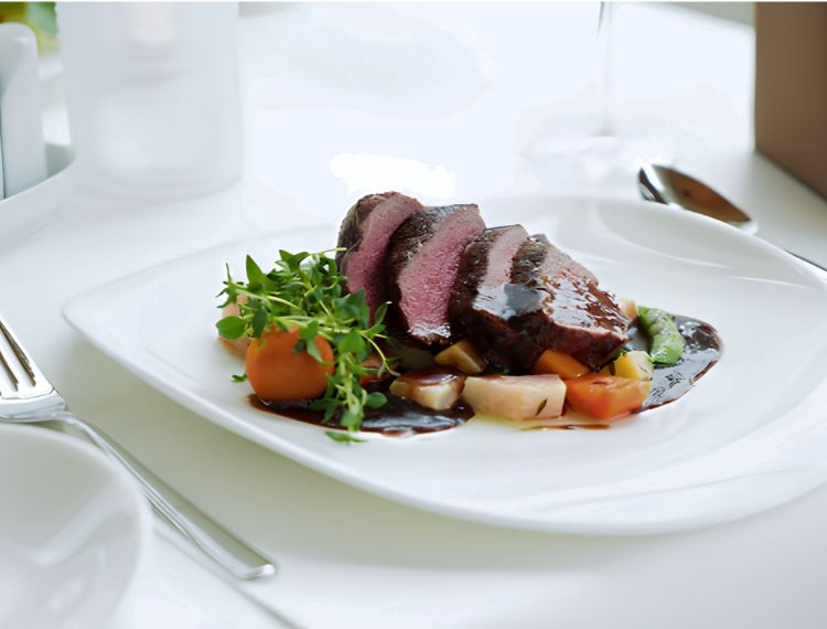 Plated medium-rare sliced beef fillet steak with dark jus reduction sauce and steamed vegetables.