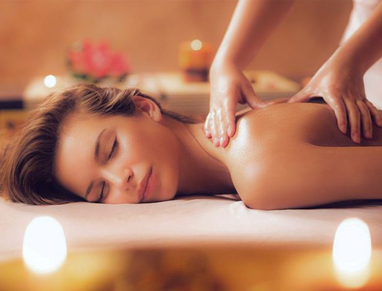 Woman resting comfortably on a massage table while receiving a back massage near soft candlelight.