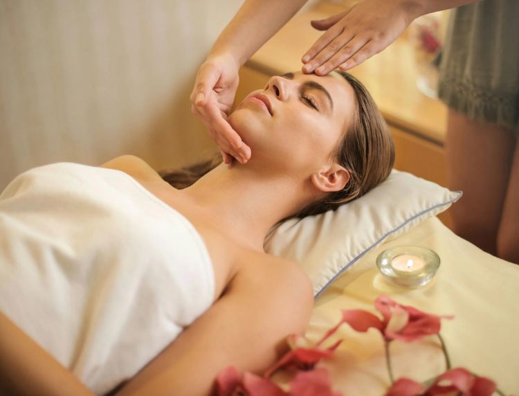 Woman receiving a relaxing facial massage during a spa wellness treatment with lit candles nearby.