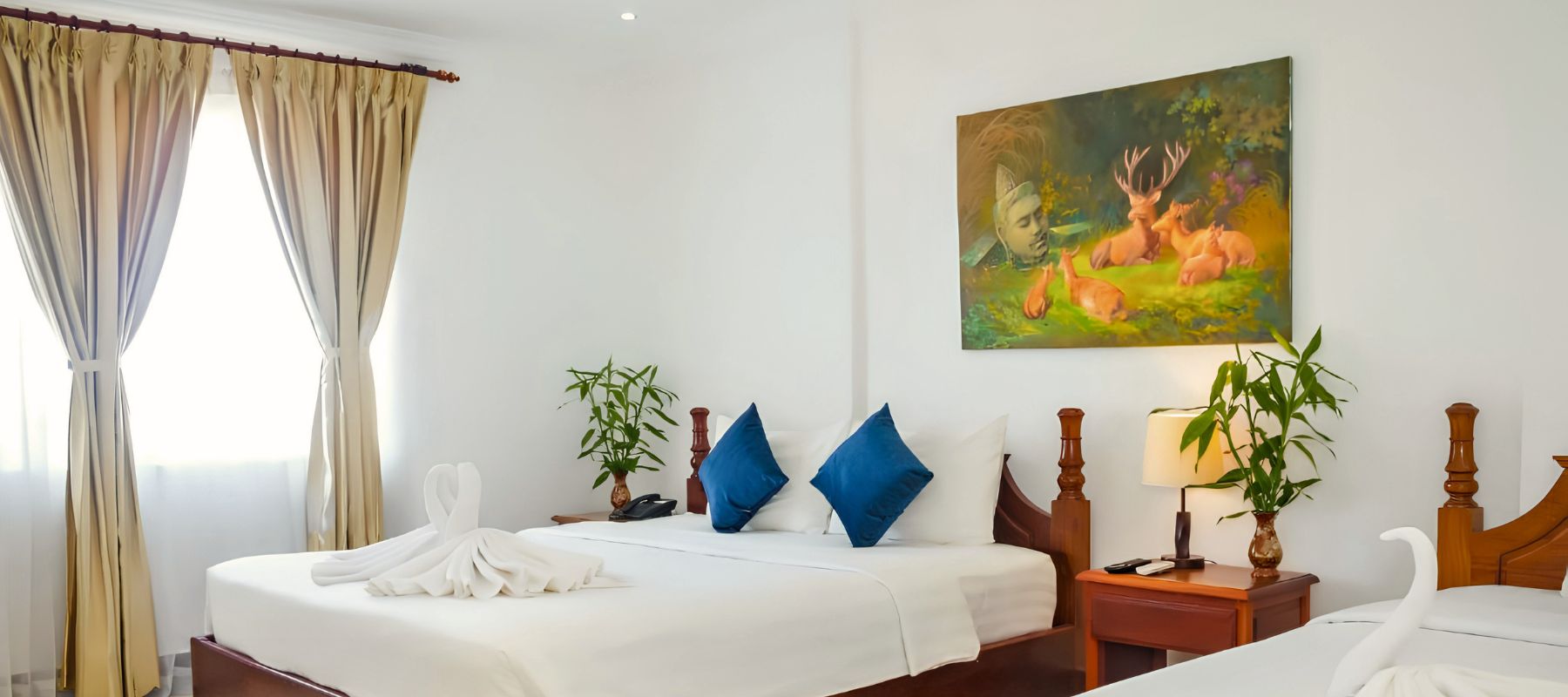 Family hotel suite bedroom featuring white linens, blue accent pillows, towel swans, and wooden nightstands.